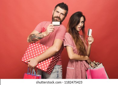 Guy With Beard And Pretty Lady Do Shopping. Couple In Love Holding Shopping Bags Shows Credit Cards On Coral Background. Man With Smile Stands Close To Woman. Shopping And Spending Habit Concept