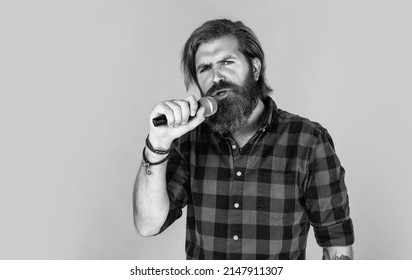 guy with beard singing in microphone. confidence and charisma on stage. bearded man wearing checkered shirt. rock music. male karaoke singer. mature charismatic male vocalist. copy space