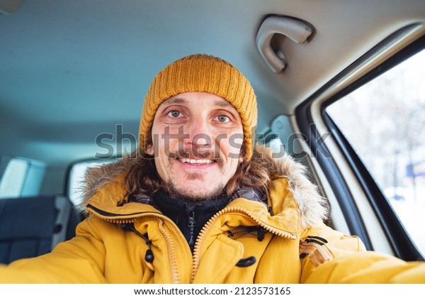 A guy with a beautiful\
big smile sits in the car. A man takes a selfie in a bright yellow\
jacket. A trip by car in winter.Havefun with yourself. High quality\
photo