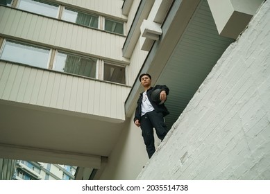 Guy In Black Holding A Basketball. Skinny Asian Guy With Black Ball Standing Against Multi-storey Building, Full Body