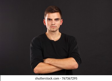 A guy in black jacket poses with his arms crossed over his chest against a black background. Indoors.