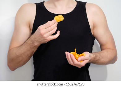 A Guy In A Black Shirt Holds Chips In His Hand. Torso And Hands Of A Man Close-up. Harmful Food For Athletes, A Snack After A Workout, An Appetizer For Beer.