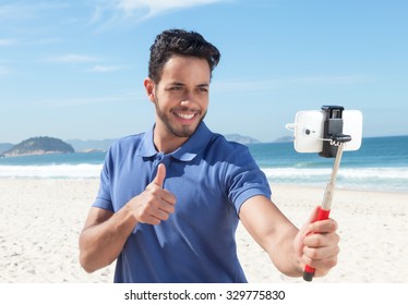 Guy With Blue Shirt And Beard At Beach Taking Selfie With Stick