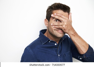 Guy in blue shirt peeking out from hand over eyes