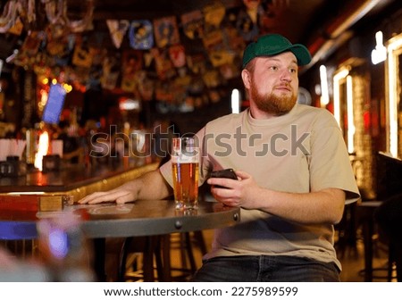 the guy in the cap is drinking beer and doing work on his phone