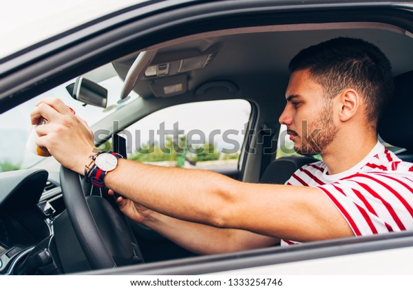 A guy in car is holding coffee in one\
hand and looking in his phone while driving\
risky