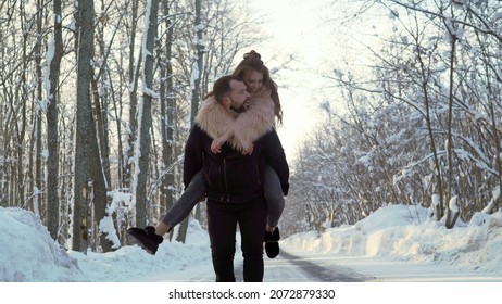 The guy is carrying a girl on his shoulders in a winter park. Beautiful young Caucasian people couple lovers on a date in winter park. Valentine's day holiday theme.