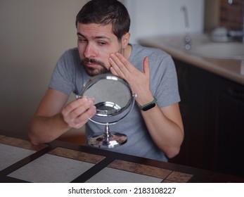 guy checking his skin. Young man looking in mirror touches face with pimple feels disgruntled. Anti-acne skincare treatment, hormonal imbalance, stress, diet, skin problem, freckle appearance concept