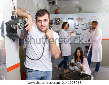 Guy checking telephone set while trying to get out with friends of escape room stylized as underground shelter