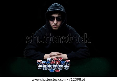 The guy in dark glasses, the player in gamblings sits at a table before it a heap poker chips
