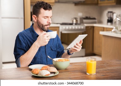 Guy in denim shirt eating cereal and drinking coffee for breakfast while reading a book on a tablet computer - Powered by Shutterstock