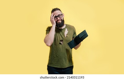 A Guy With A Dirty Face And In Torn Clothes Holds A Wallet In His Hands And Tries To Find At Least Some Money. Unemployed Economic Crisis. Inflation And Bankruptcy.