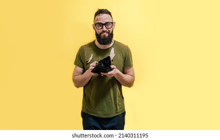 A Guy With A Dirty Face And In Torn Clothes Holds A Wallet In His Hands And Tries To Find At Least Some Money. Unemployed Economic Crisis. Inflation And Bankruptcy.