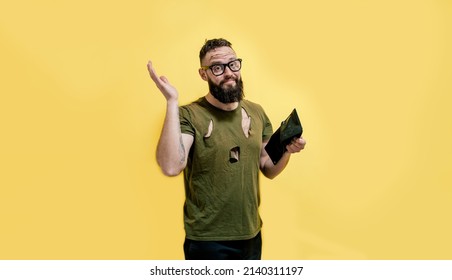 A Guy With A Dirty Face And In Torn Clothes Holds A Wallet In His Hands And Tries To Find At Least Some Money. Unemployed Economic Crisis. Inflation And Bankruptcy.