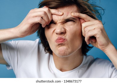 A guy with disheveled hair squeezes acne on his forehead in a white T-shirt - Shutterstock ID 1348673177