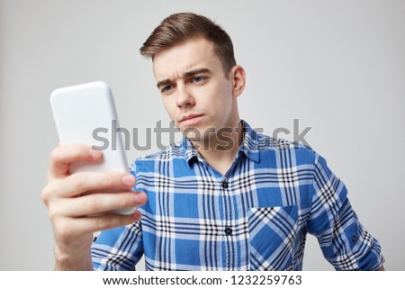 A guy dressed in a plaid shirt looks seriously at his mobile phone on a white background in the studio
