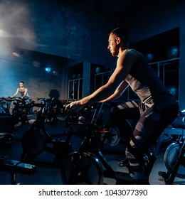 The guy is engaged in a bicycle simulator in the gym. Toned image. The guy is exercising on a stationary bike. in side with reflection