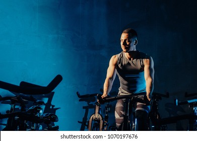 The guy is engaged in a bicycle simulator in the gym. Toned image. The guy is exercising on a stationary bike. portrait in the front view