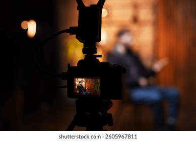 A guy is engaged in an interview while sitting on a chair, speaking directly to the camera. The warm-toned background creates an inviting atmosphere for the podcast discussion.