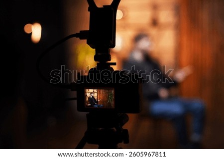 A guy is engaged in an interview while sitting on a chair, speaking directly to the camera. The warm-toned background creates an inviting atmosphere for the podcast discussion.