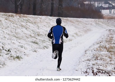 The Guy Is Engaged In Jogging In Sportswear In The Winter Nature. Extreme Weather Conditions For Sports And A Healthy Lifestyle. Tracking Training On A Snowy Road. Preparation For The Competition