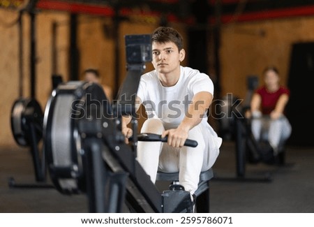 Guy exercises on a rowing machine in the gym. European man is preparing for the rowing competition. Fitness club client at a group cardio workout