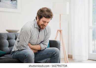 Guy feeling unwell with a stomach ache while sitting at home - Shutterstock ID 1627967734