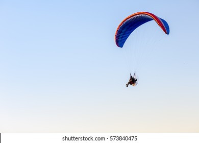 Guy flying on the clearly blue sky and wonderful beach by paramotor red kite,extreme activity port. feel freedom like birds. concept overcome the limits of  human physiology.