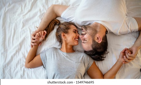 Guy and a girl in a cozy home environment. Happy man and woman lying in the bedroom stock photo. Top view of smiling young couple cuddling in bed in morning.  Beautiful pair of lovers hug and kiss - Powered by Shutterstock