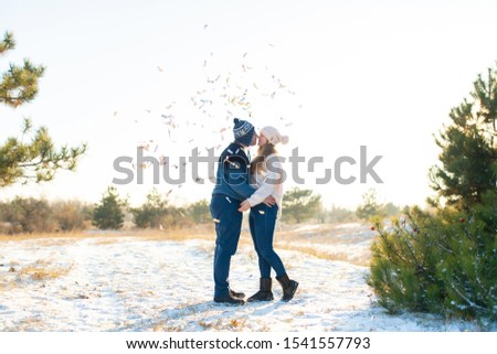 The guy with the girl kiss in the winter in the woods against the background of falling candy. Romantic winter atmosphere.