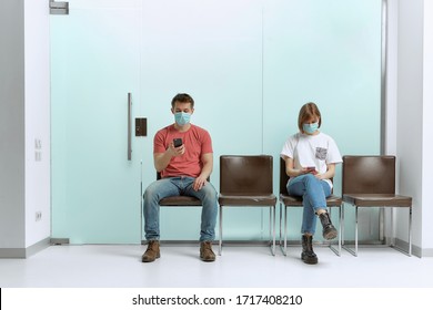 A guy and a girl in medical masks, sitting in a queue, and waiting for a doctor's appointment in the hospital.