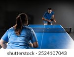 A guy and a girl are playing table tennis against each other. Blue table tennis and black background