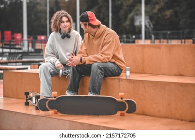 Guy and girl with skateboards talking sitting in park