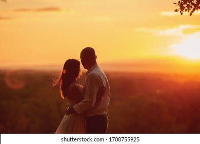 Guy girl stand in an embrace and look at the beautiful red-orange sunset and the rays of the sun. - Powered by Shutterstock