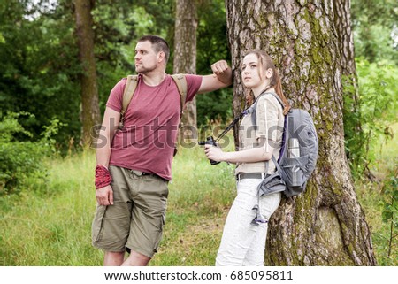 Guy with a girl, a young couple traveling with backpacks on the wild, having a rest standing at a tree