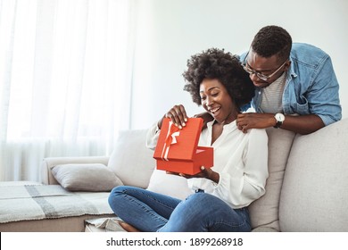 The guy gives a gift box to his girlfriend. Young couple on holiday. St. Valentine's Day. Smiling mid adult man surprising his girlfriend with a gift.  Couple celebrating Valentines day anniversary  - Shutterstock ID 1899268918