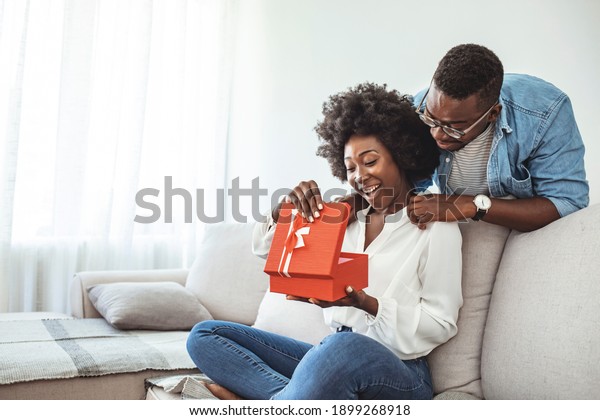 The guy gives a gift box to his girlfriend.\
Young couple on holiday. St. Valentine\'s Day. Smiling mid adult man\
surprising his girlfriend with a gift.  Couple celebrating\
Valentines day anniversary 