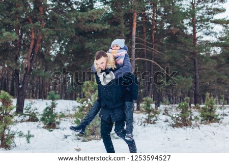 Guy giving his girlfriend piggyback in winter forest. Youn loving couple having fun outdoors