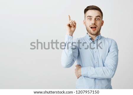 Guy got excellent idea sharing with team. Enthusiastic excited good-looking male in formal blue shirt raising index finger in eureka gesture holding breath and opening mouth while adding suggestion