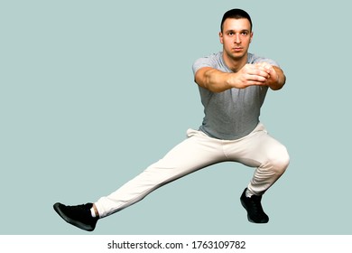 Guy In Grey Shirt And White Sweat Suit Stretching His Right Leg With His Arms In Front, Isolated