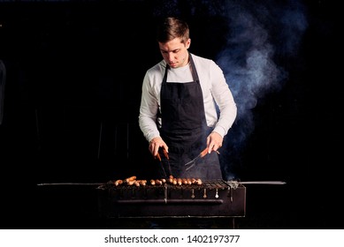 The Guy Is Grilling Sausages In An Apron