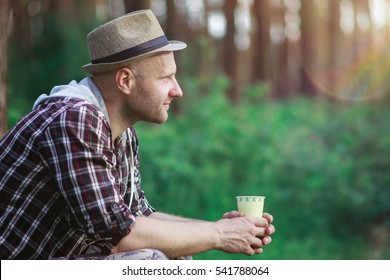 guy in a hat sitting in the forest rest and drink from the cup of coffee