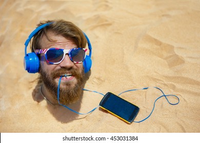 Guy with headphones buried in the sand on the head