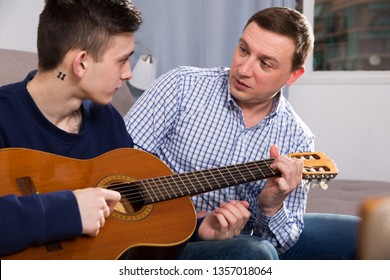 Guy With His Father Are Resting And Playing On Guitar At The Home.