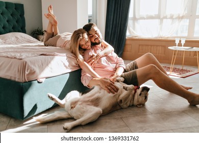 Guy and his girlfriend are resting in bedroom. Happy couple lovingly looking at their pet who wants to play