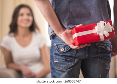 Guy Is Holding Gift Behind Him Is Trying To Surprise His Is Waiting Girlfriend At Home. Focus On Boy.