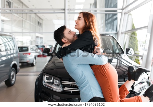 Guy hugs his girlfriend in a car dealership\
on the background of a purchased\
car
