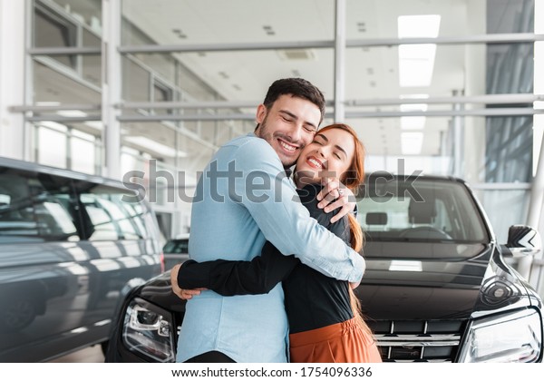 Guy hugs his girlfriend in a car dealership\
on the background of a purchased\
car