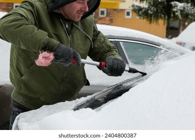 guy in jacket, hat and gloves scrapes car windows from ice to blizzard - close up view.