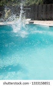 Guy Jumps Into An Outdoor Swimming Pool In The Summer. Man Lands In Pool From Jumping Off Diving Board Doing Cannon Ball Into A Pool With Big Splash As He Lands In The Deep End Of The Pool.